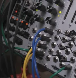 Modular system with silver panels with black knobs, yellow, red, and orange lights, grey, green, yellow, and blue cables